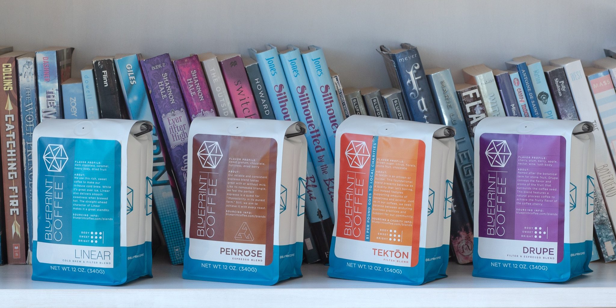 12oz bags of the four primary Blueprint Coffee blends in front of a filled bookshelf
