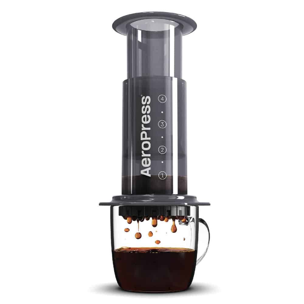 The aeropress coffee brewer sits atop a mug of coffee, which is translucent and shows brewed coffee dripping from the brewer into the cup.
