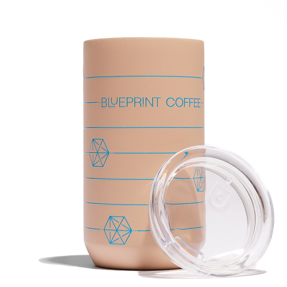 A 12-ounce sandy brown Blueprint Coffee "cube" tumbler against a white background. The tumbler is a sandy brown color with blue print. The lid rests against the side.