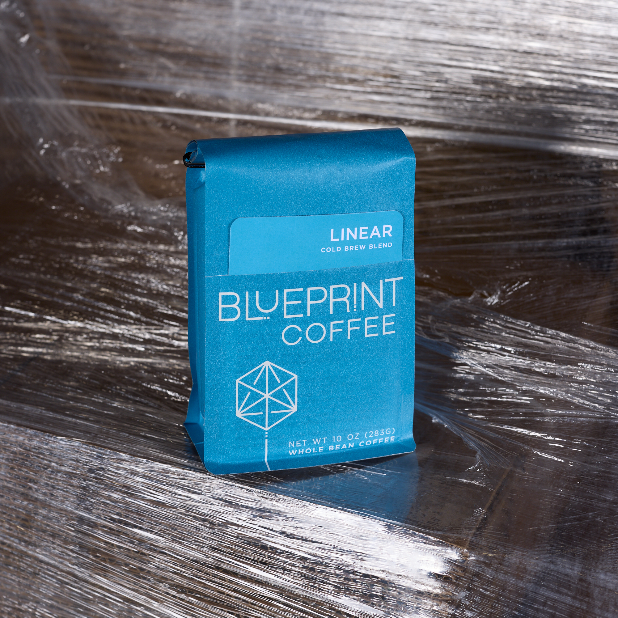 A blue 10-ounce bag of Linear Cold Brew & Filter Blend stands on a plastic-wrapped pallet