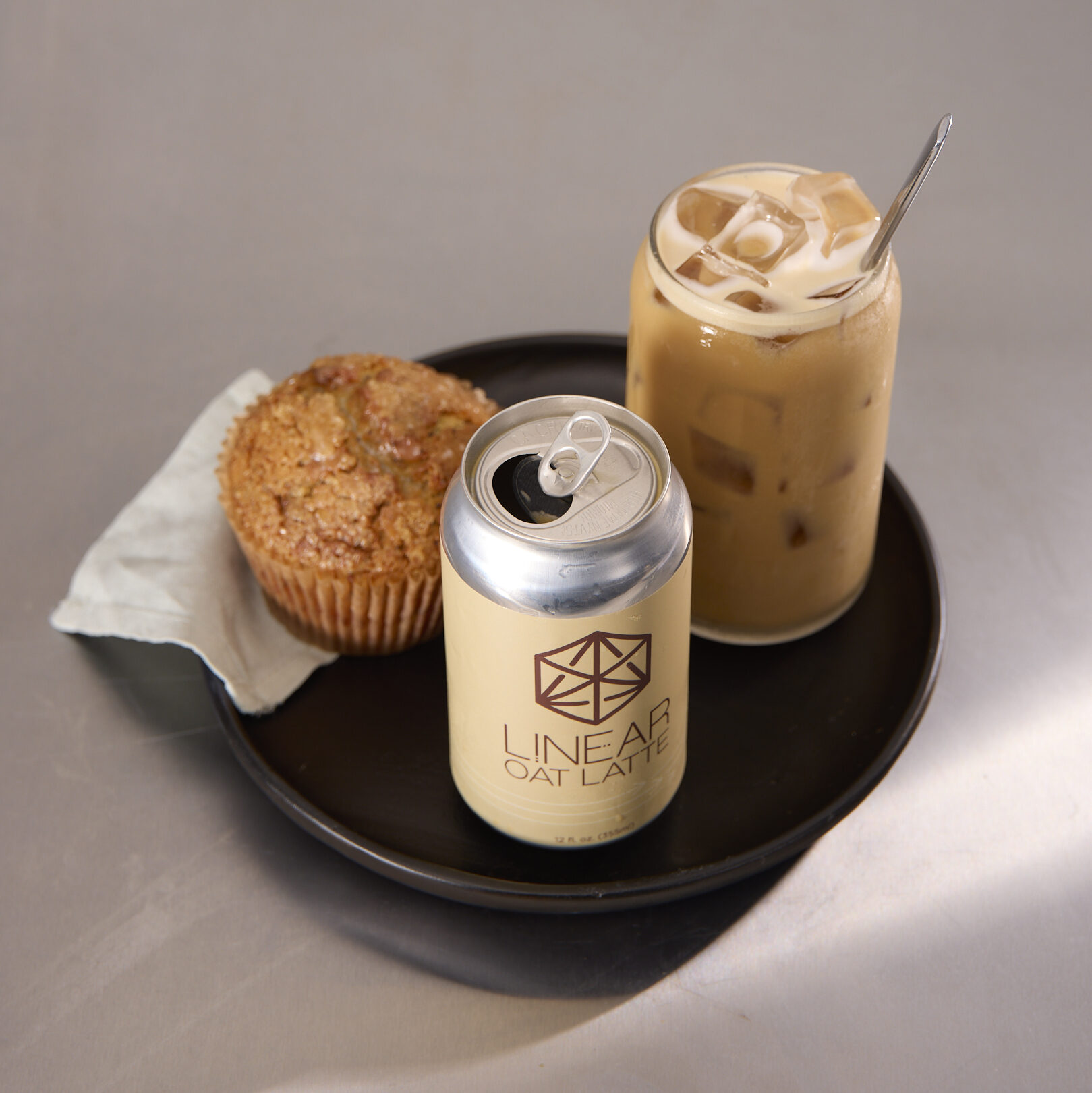 A can of Linear Oat Latte arranged on a tray with a glass of oat latte and a muffin