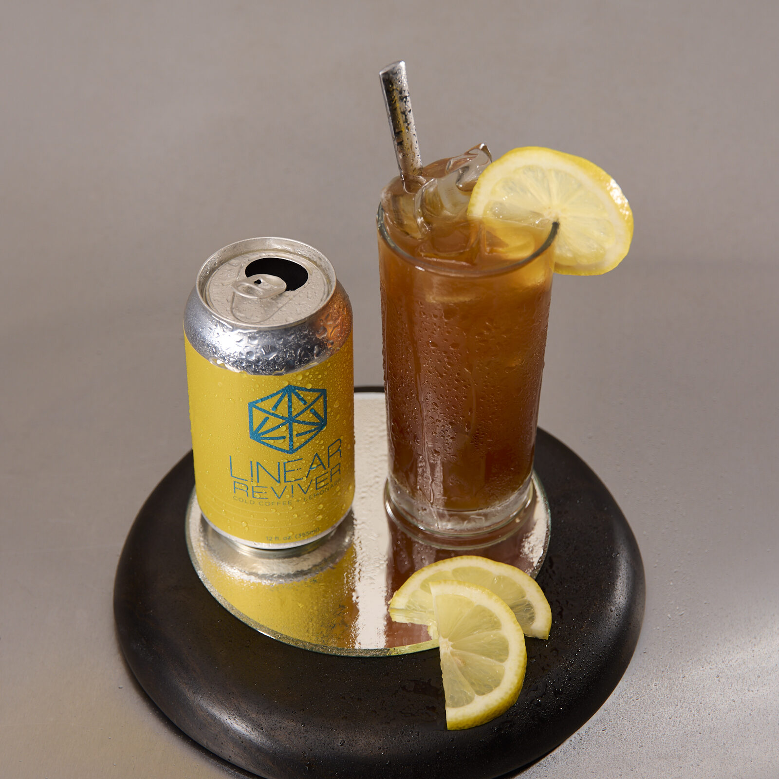 A glass of Linear Reviver arranged on a tray beside its empty yellow can and slices of lemon