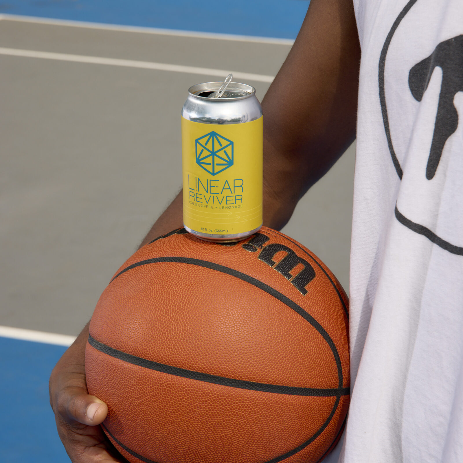 A man holds a basketball at his side with a yellow can of Linear Reviver balanced on top