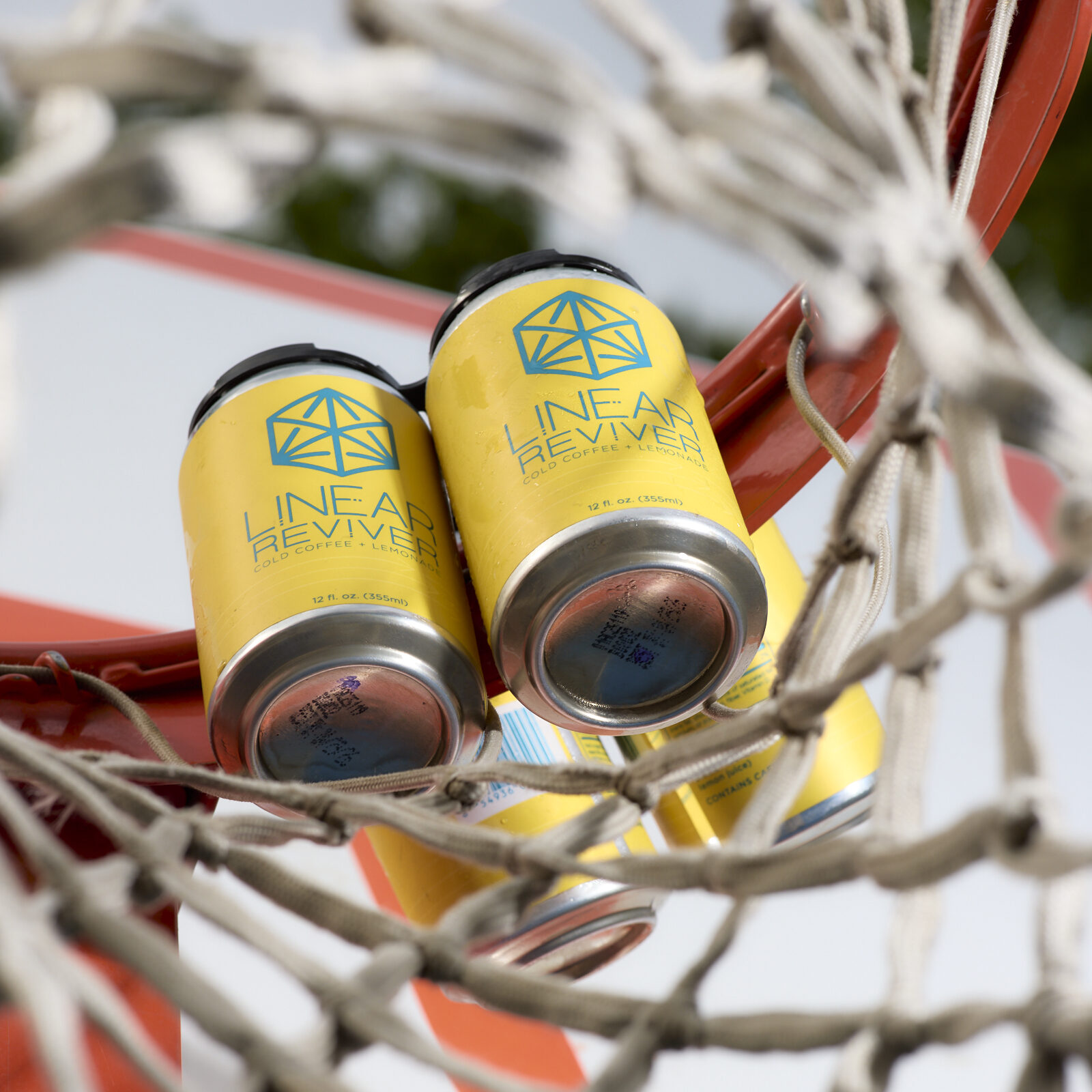 A 4-pack of Linear Reviver cans is placed atop the orange rim of a basketball net and views from below